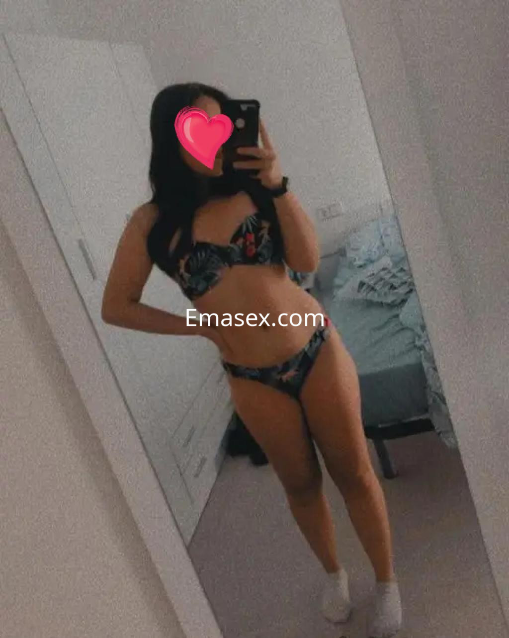 Escort en Salamanca se refleja en un espejo, vistiendo un bikini colorido, con cabello oscuro y lacio.