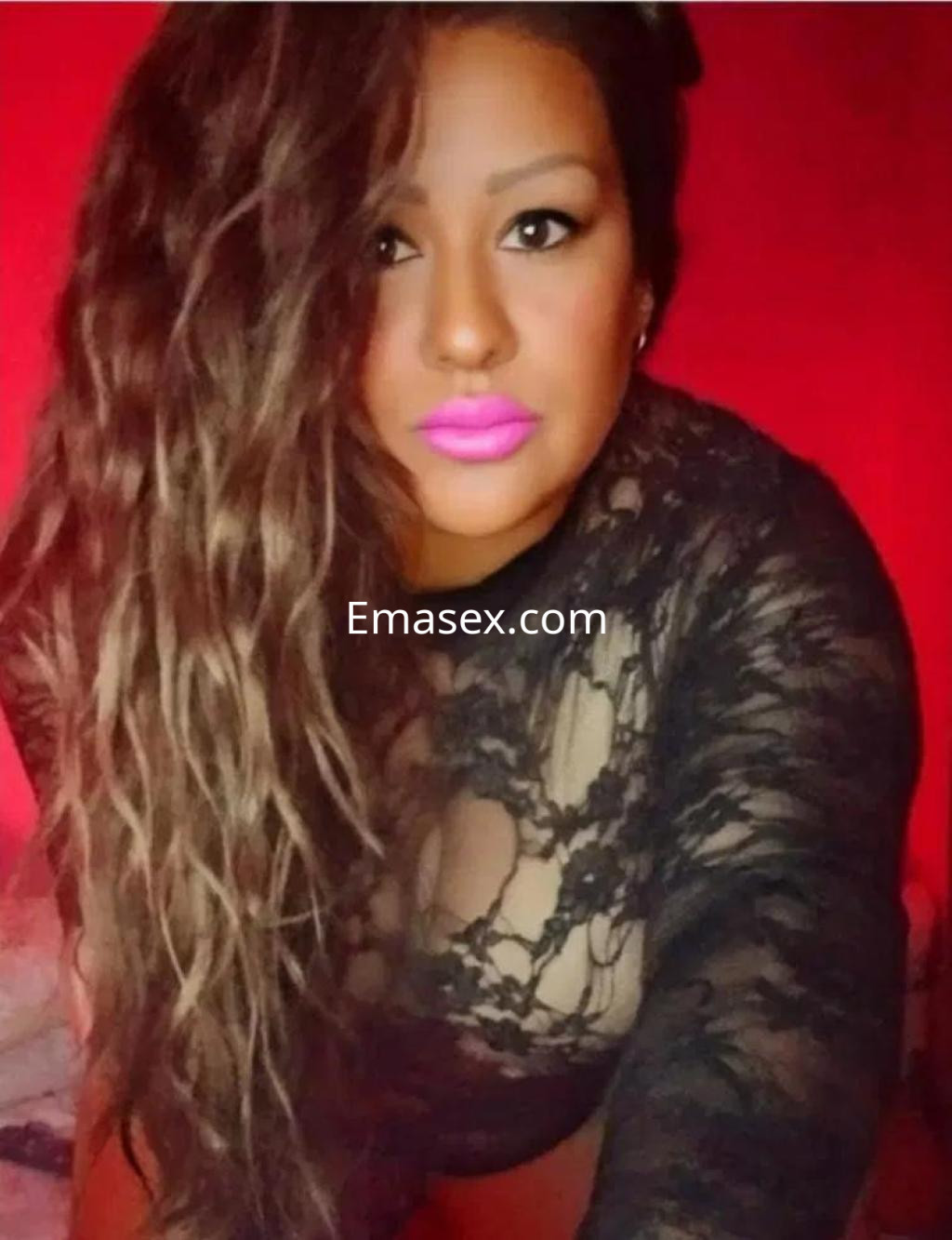 Escort en Valencia con cabello largo y ondulado, usando un top de encaje negro y labial rosa brillante.