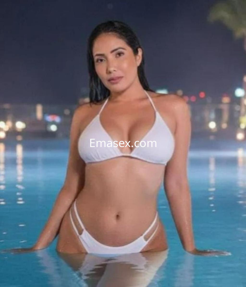 Escort en Alicante, de cabello oscuro y lacio, luciendo un bikini blanco en una piscina iluminada.