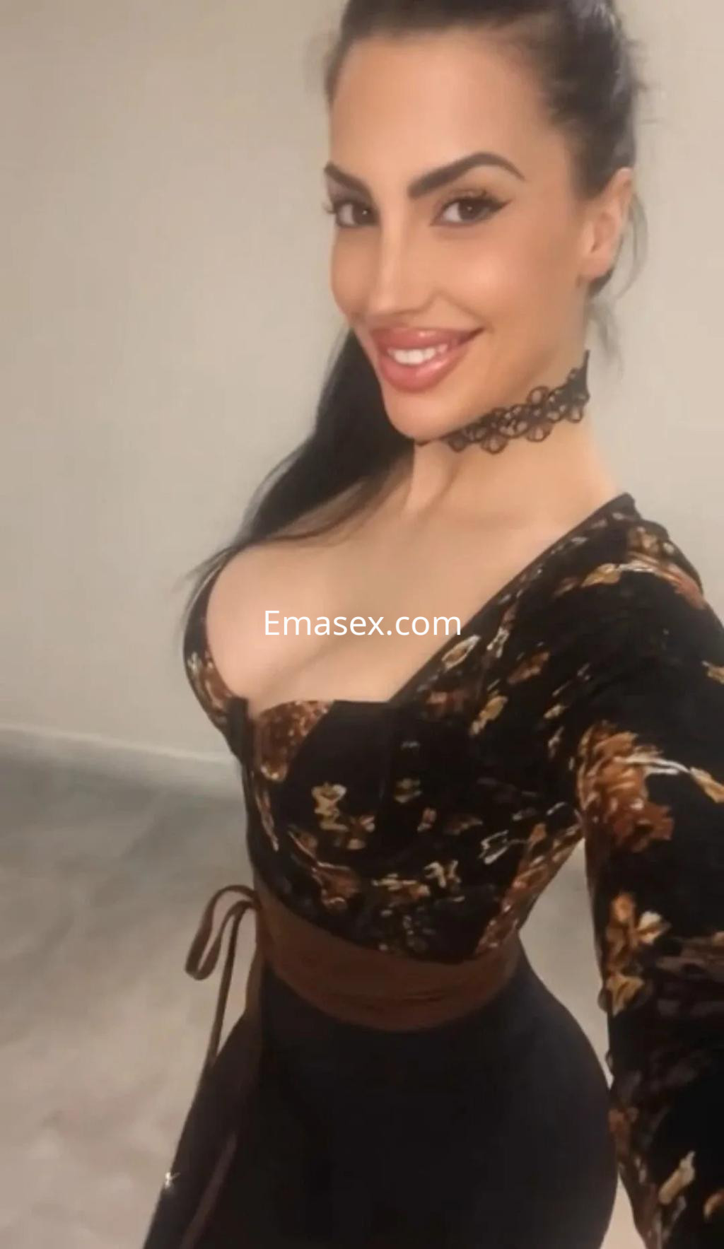 Escort en Alicante con cabello oscuro y lacio, vestida con blusa ajustada de estampado floral y cinturón.