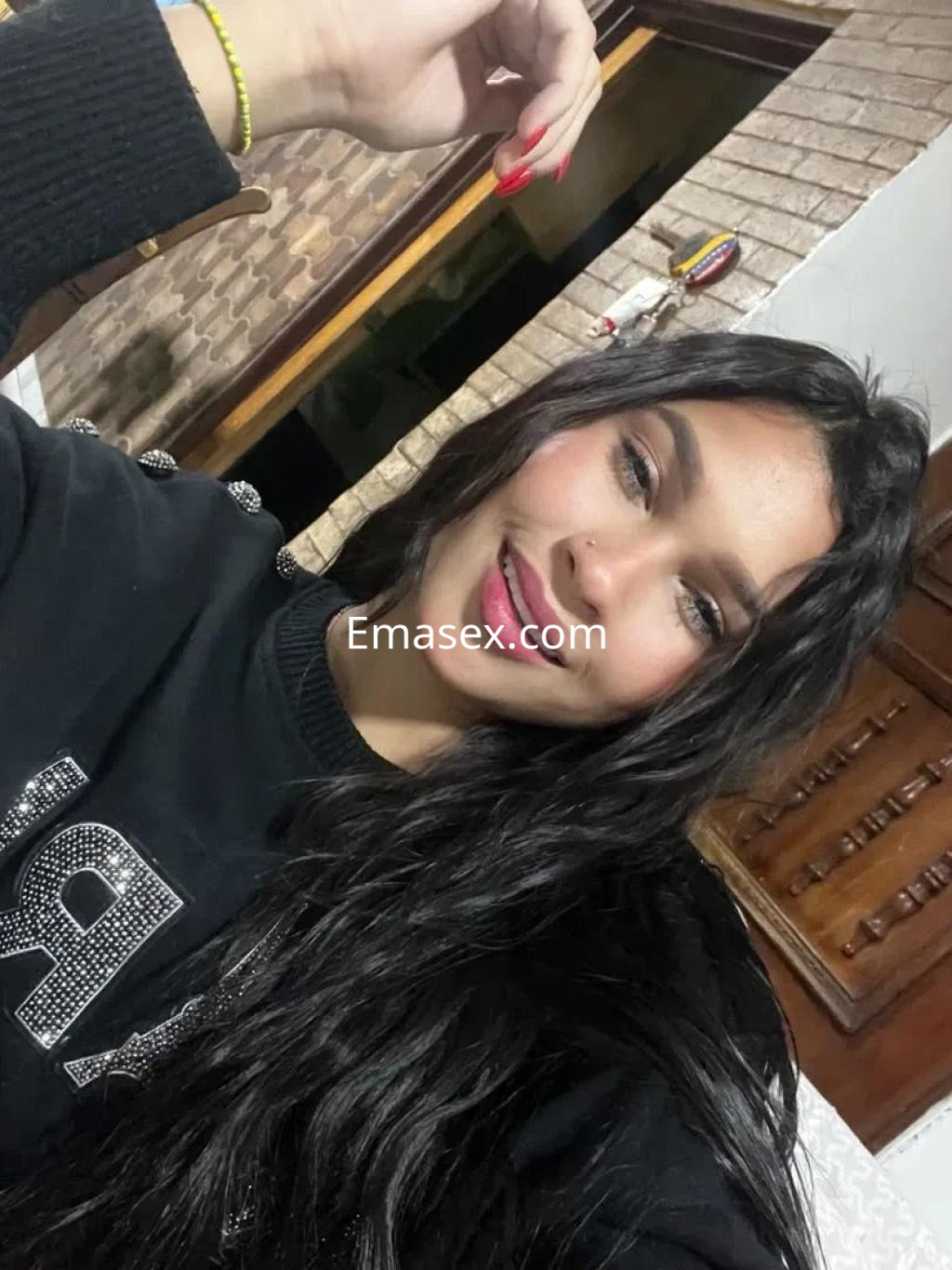 Escort en Barcelona con cabello largo y oscuro, sonríe mientras lleva un suéter negro en un ambiente interior.
