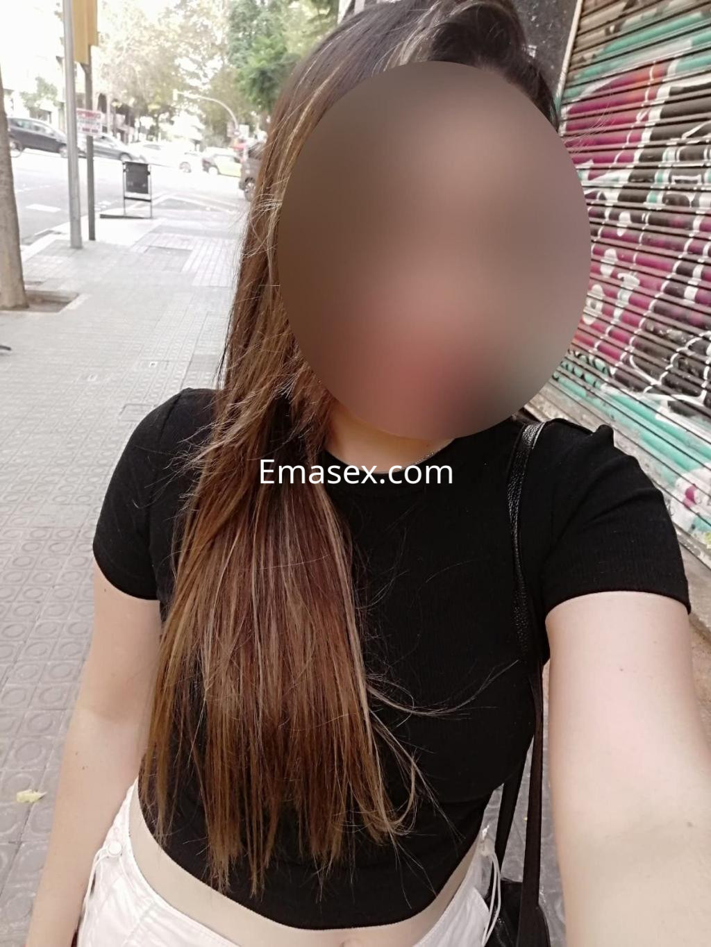 Puta en Barcelona con cabello largo y lacio, viste una blusa negra y una falda clara, posando en la calle.