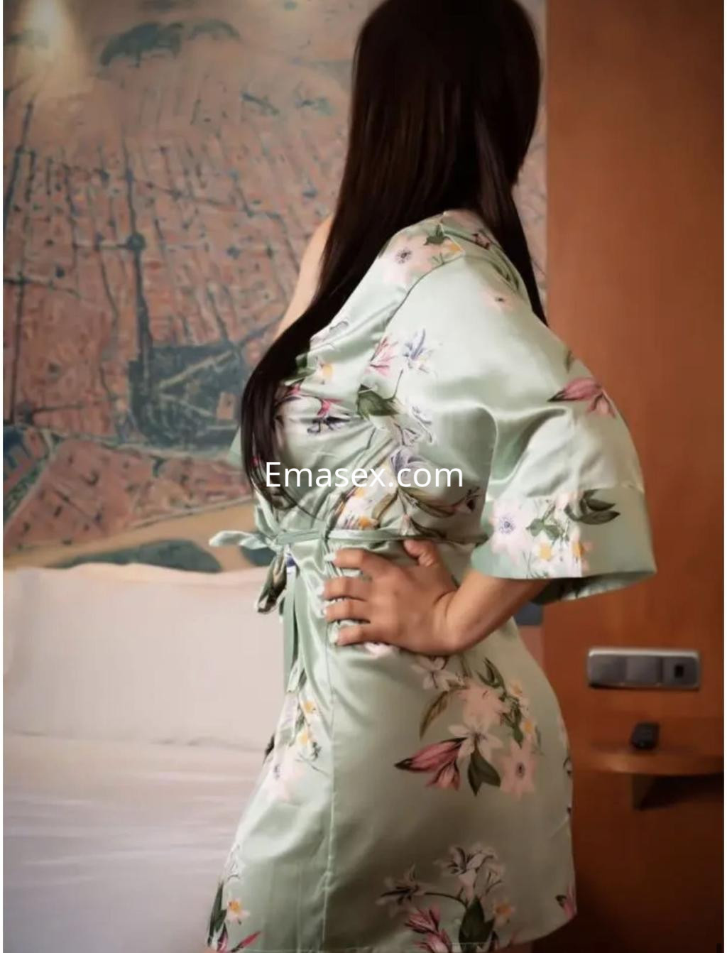 Puta de cabello largo y oscuro, vestida con un kimono verde claro con flores, posando en una habitación en Cádiz.