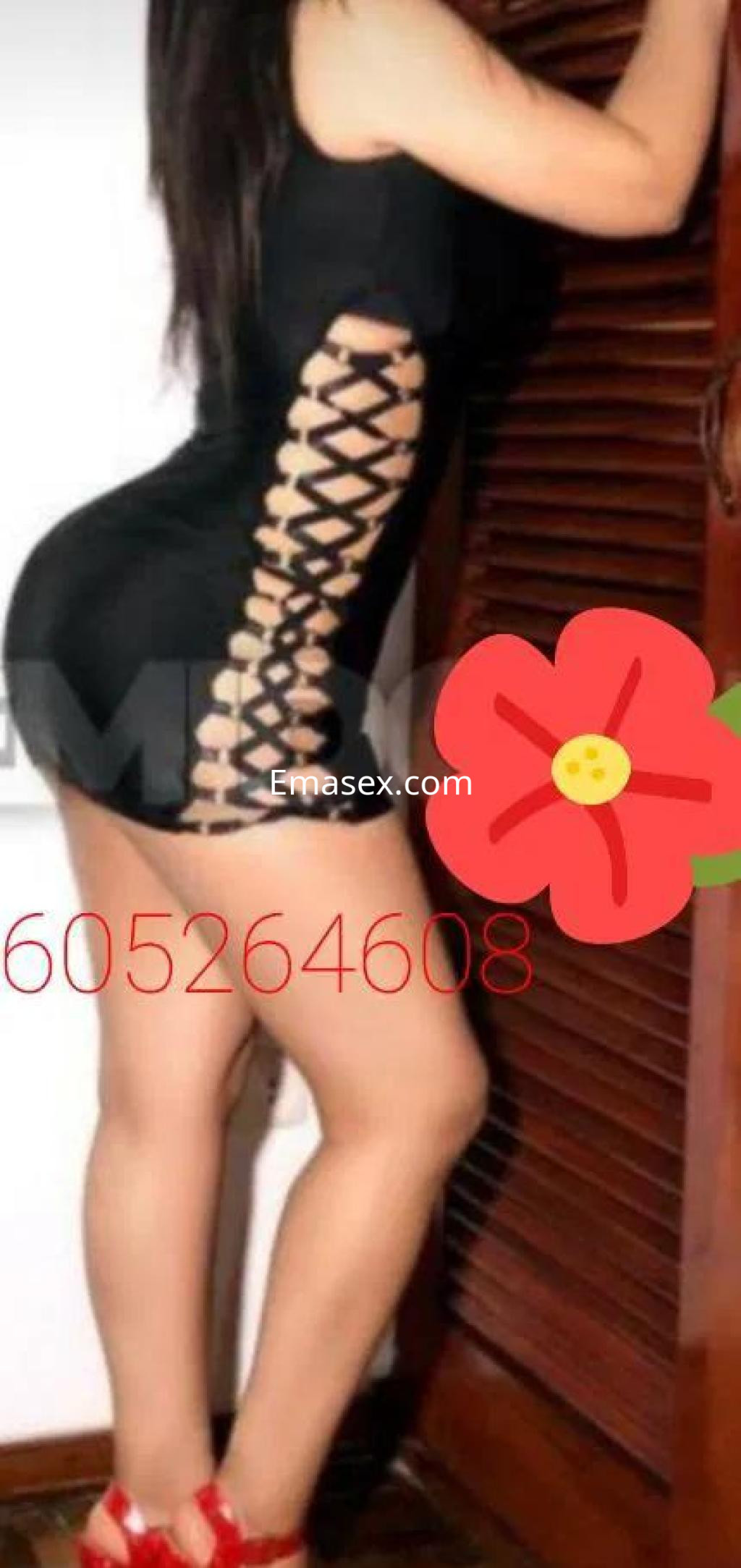 Escort en Lugo posa de perfil, luciendo un vestido negro ajustado con detalles de encaje y sandalias rojas.