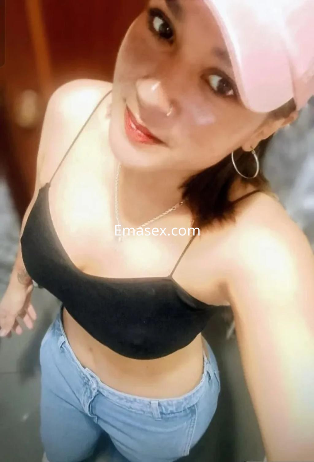 Escort en Oviedo con top negro, jeans claros y gorra rosa, sonríe mientras posa en un ambiente casual.