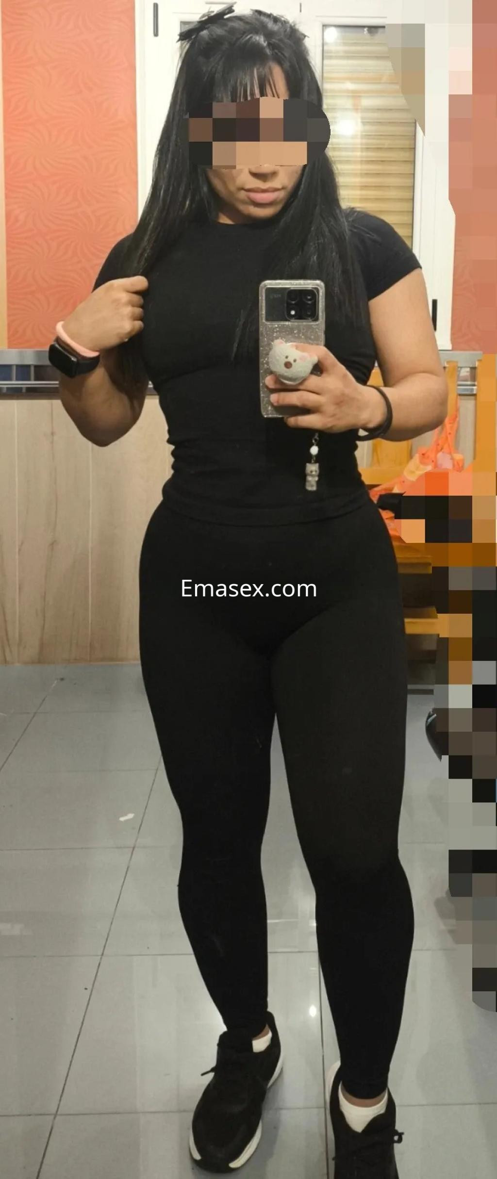 Puta en Oviedo se muestra en un espejo, vistiendo una camiseta negra ajustada y leggings oscuros, con cabello largo y lacio.