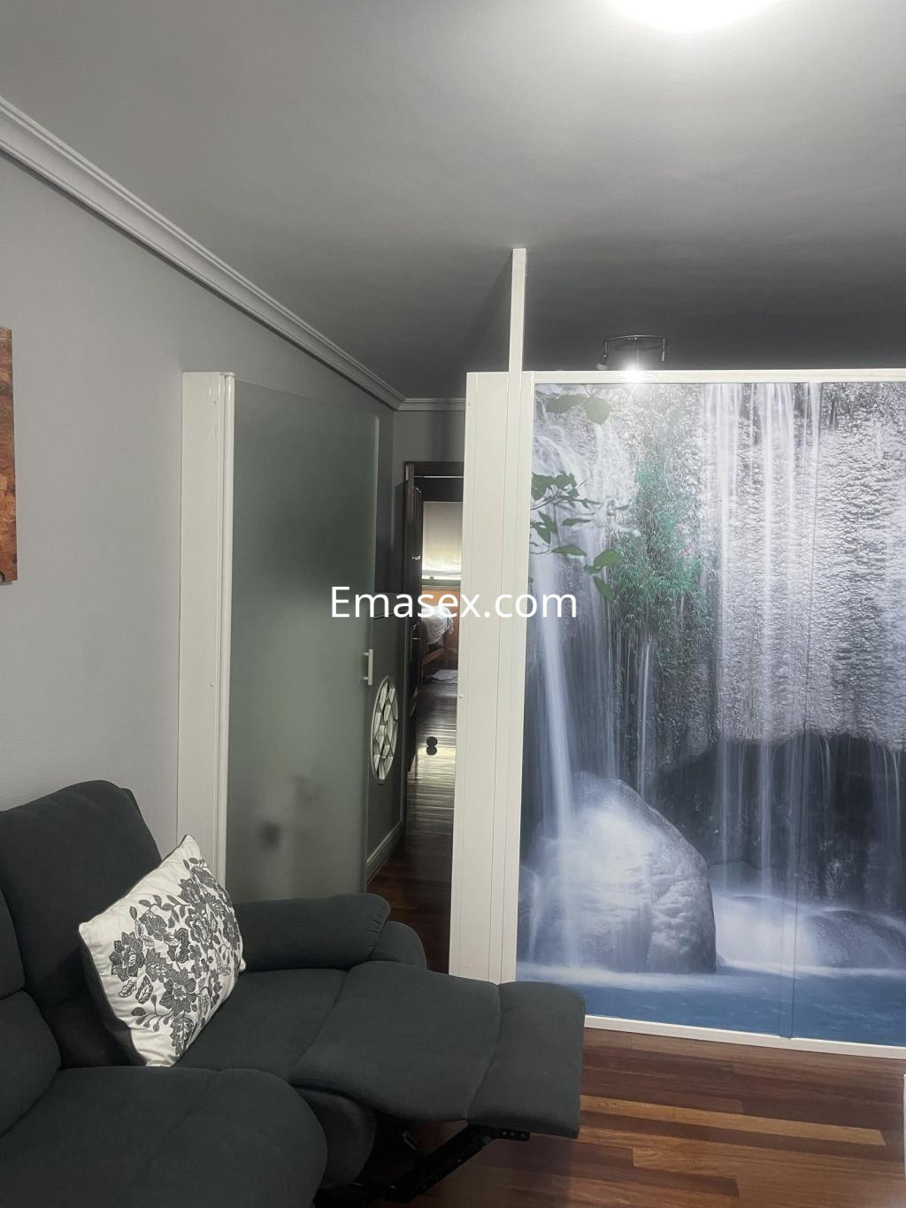 La foto muestra un interior en Vigo con un sofá gris y una pared decorativa que simula una cascada.