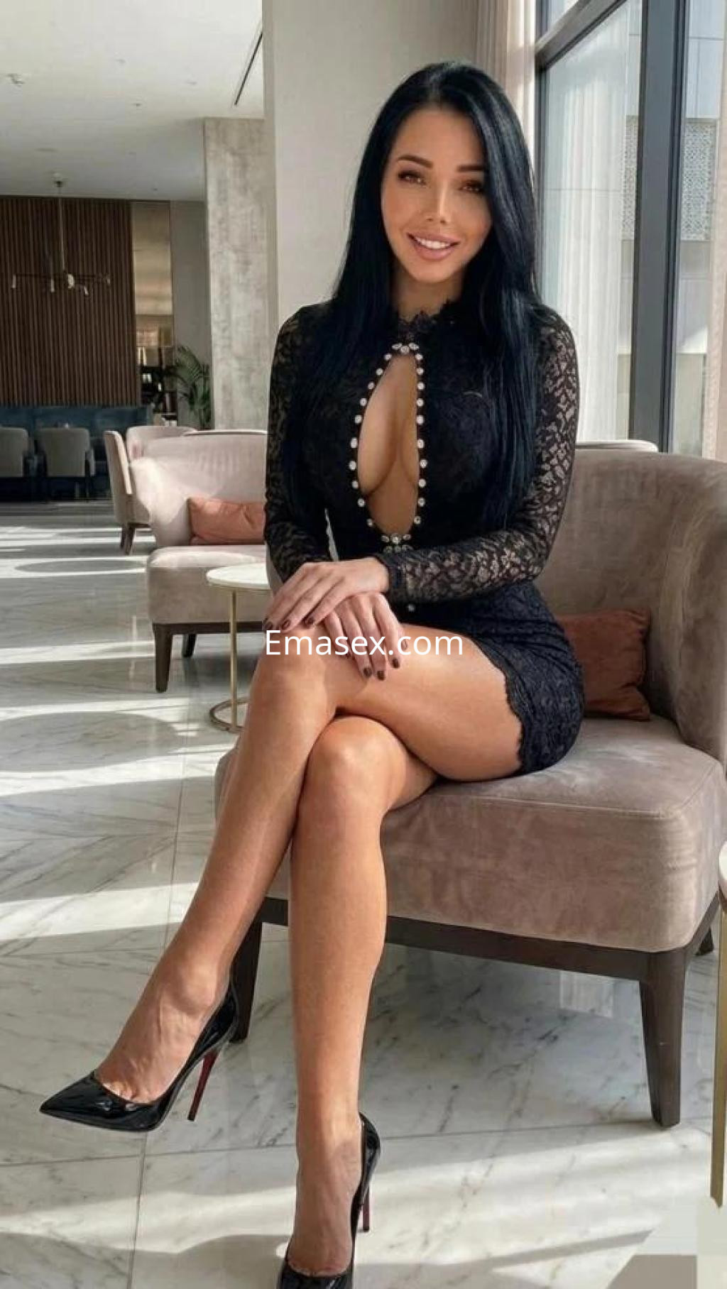 La puta luce un vestido negro de encaje con un escote profundo, sentada en un sofá en Tarragona.