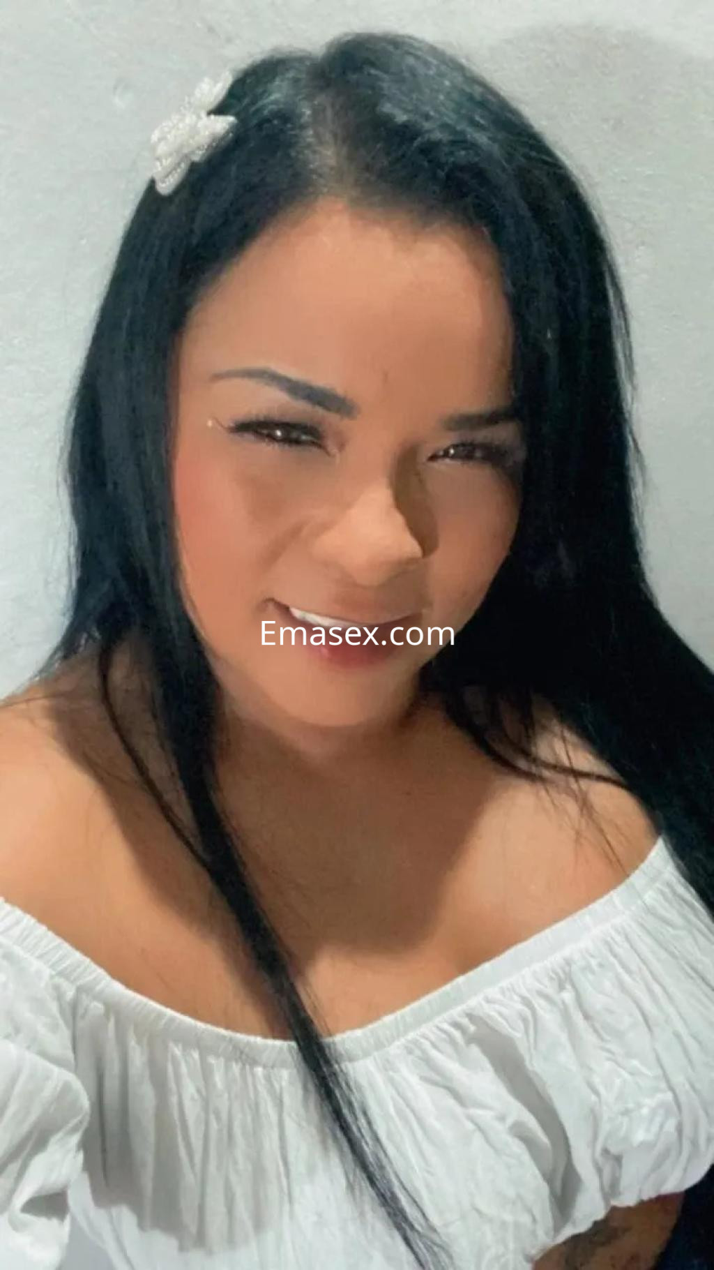 Puta con cabello largo y lacio, vistiendo blusa blanca, sonríe en un entorno sencillo en Valencia.