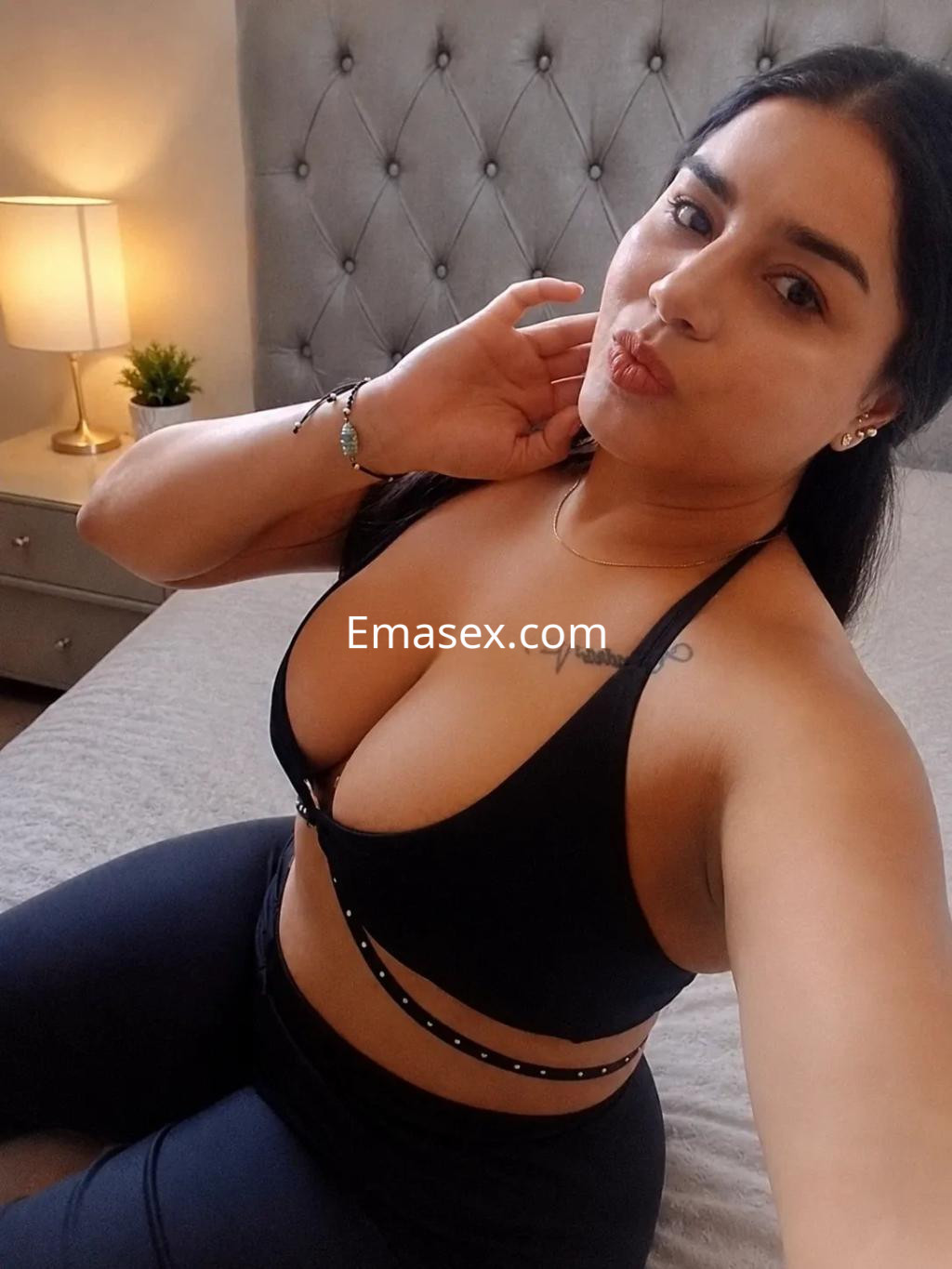 Escort en Bilbao, posando con una blusa negra ajustada y leggings, en un ambiente acogedor y bien iluminado.