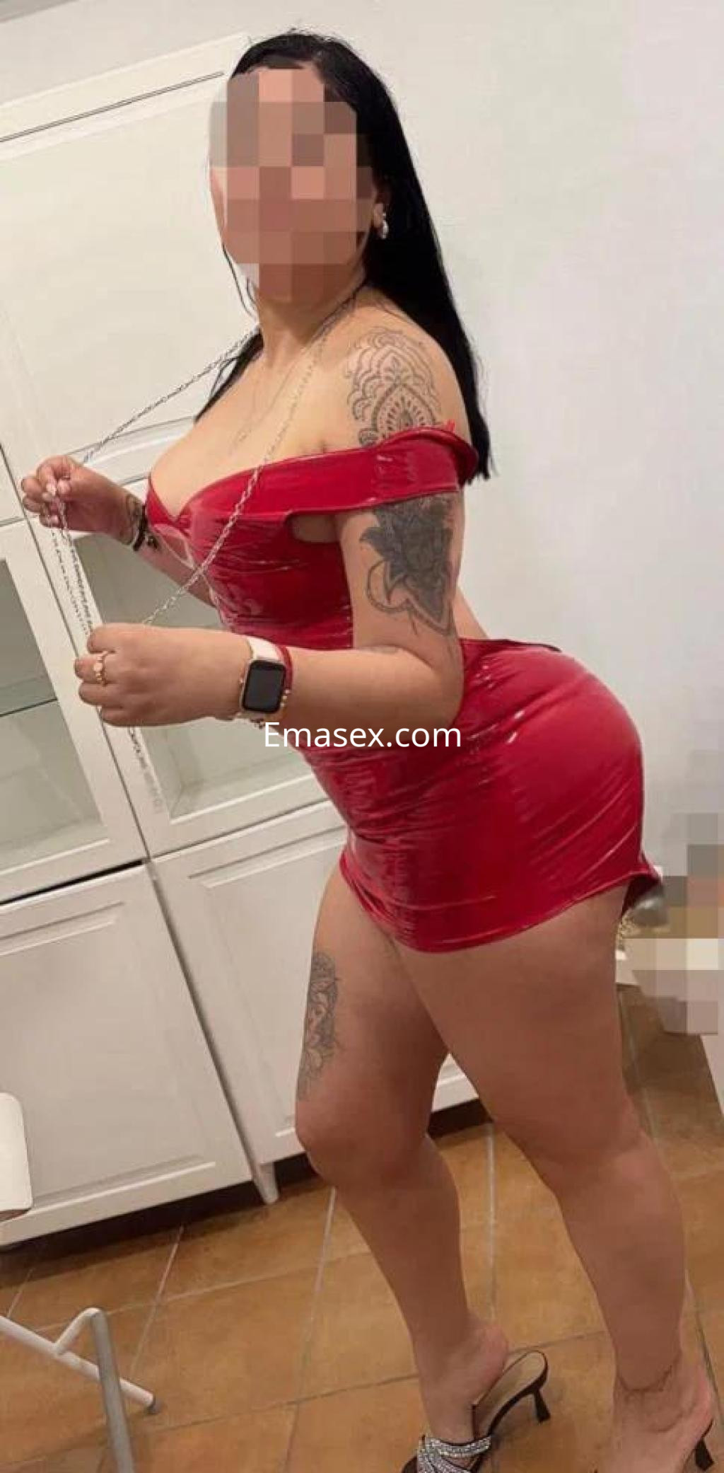 Puta en Bilbao con vestido rojo ajustado, mostrando tatuajes y posando de lado en un ambiente interior.