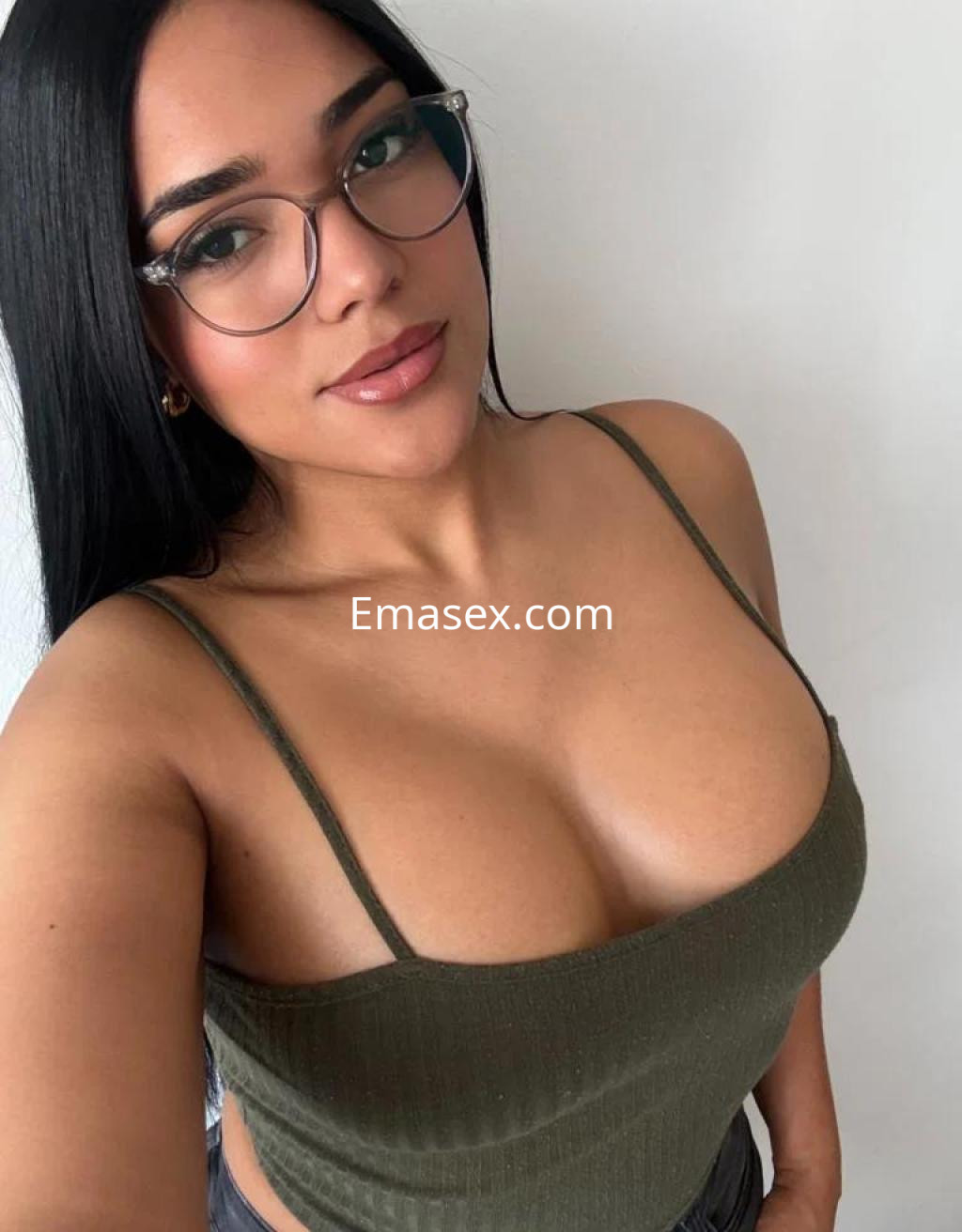 Puta con cabello largo y oscuro, usa gafas y una blusa verde ajustada, posa con una expresión seductora en Zaragoza.