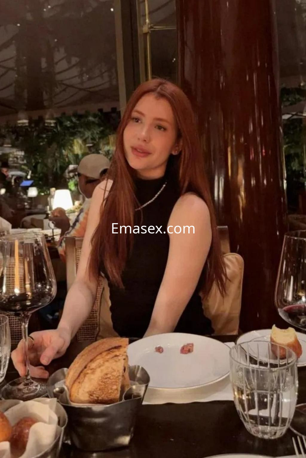 Escort en Madrid con cabello largo y castaño, vistiendo un top negro en un elegante restaurante.