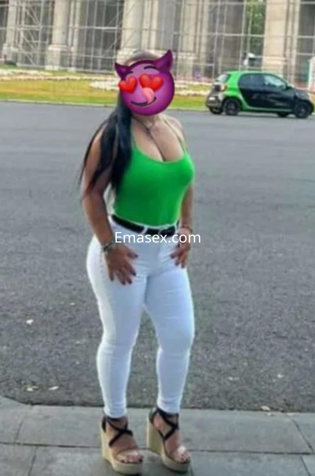 Puta de Logroño posando con un body verde y pantalones blancos, luciendo sandalias de plataforma y cabello largo.
