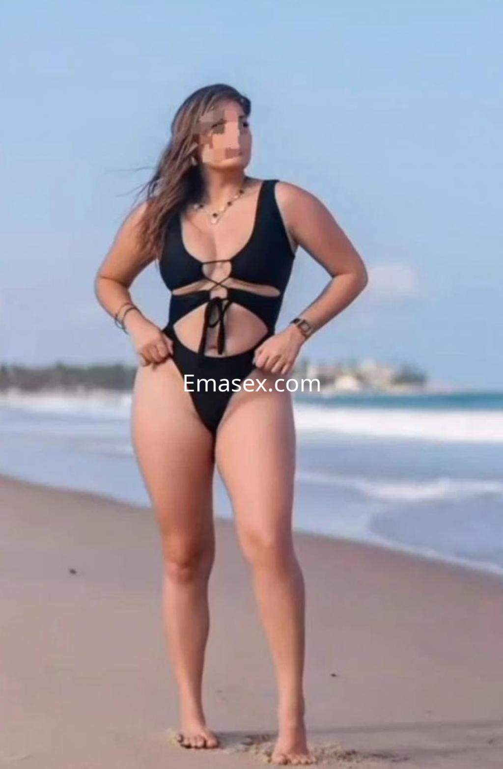 Escort en Cádiz luciendo un bañador negro de corte alto mientras posa en la playa con el mar de fondo.
