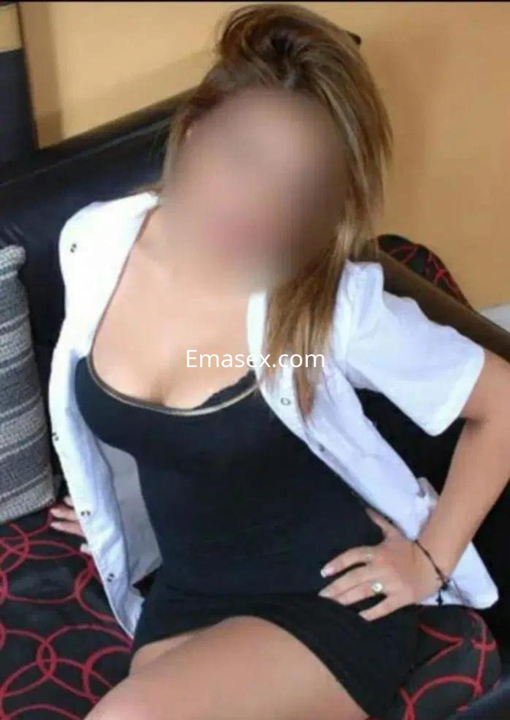 Puta sentada en un sofá, vistiendo un vestido negro ajustado y una blusa blanca abierta, con cabello largo y rubio.