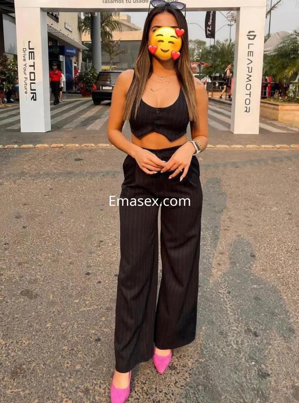 Escort en Cádiz con cabello largo y lacio, vistiendo un conjunto de dos piezas negro y zapatos rosas.