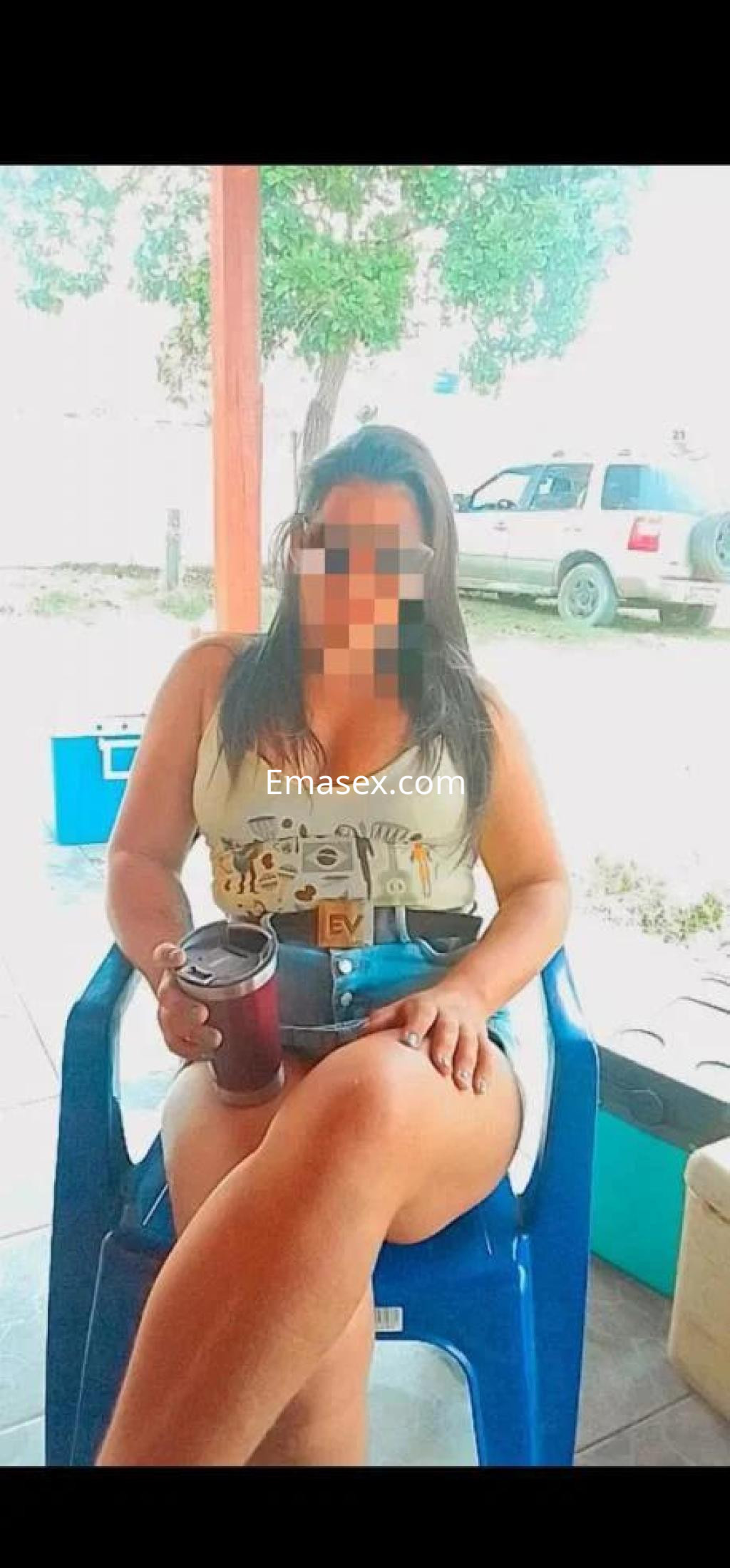 Escort en Lugo sentada en una silla, viste una camiseta clara y shorts, sosteniendo un vaso en la mano.