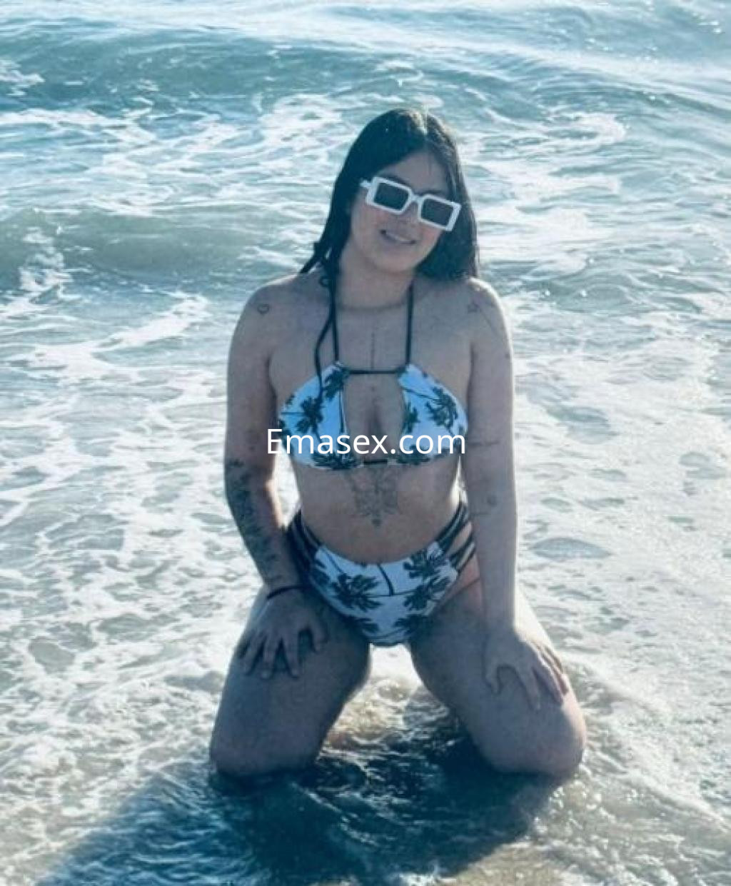 La puta está de rodillas en la playa de Pontevedra, vistiendo un bikini blanco con estampado de palmeras.
