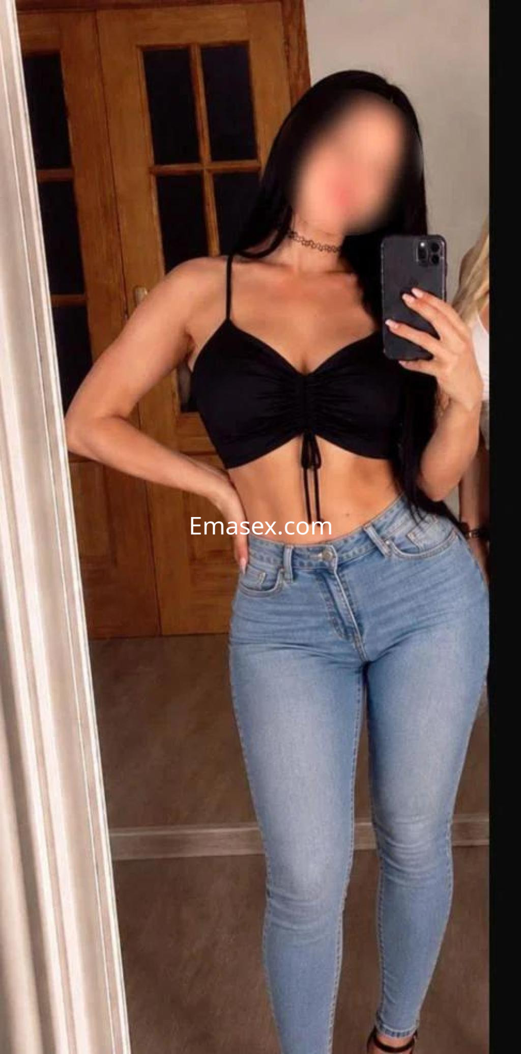 Puta en Tarragona posando en un espejo, viste un top negro y jeans ajustados, mostrando su figura.