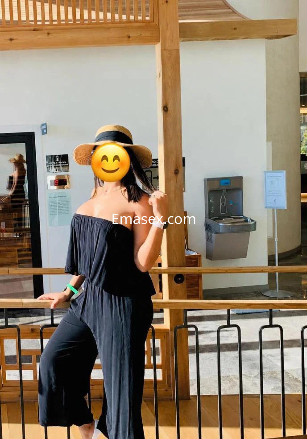 Puta en Toledo luce un conjunto negro sin mangas, con sombrero, posando en un ambiente moderno y luminoso.