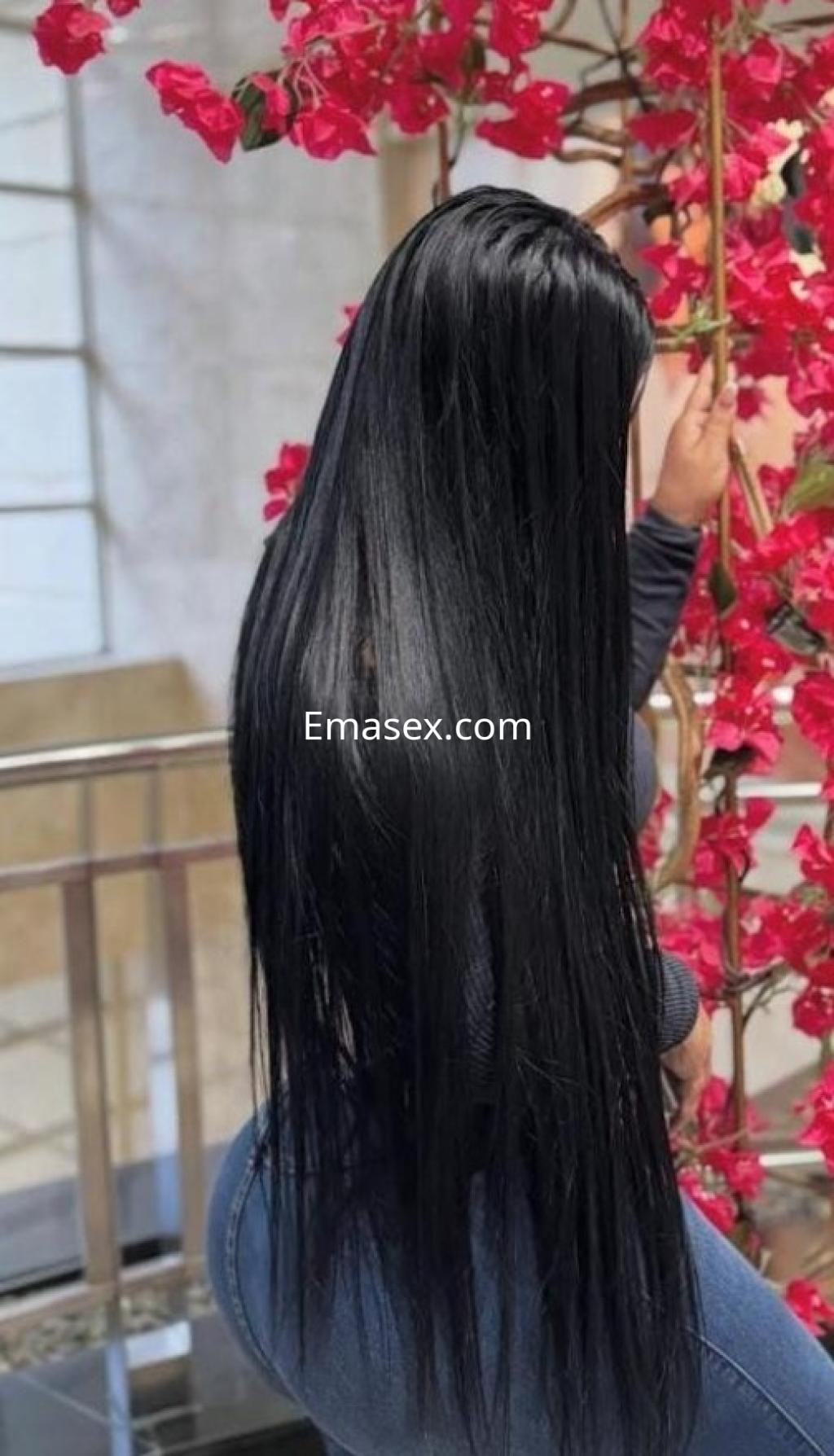 Escort con cabello largo y lacio, vistiendo un ajustado atuendo gris, posa junto a flores en Vigo.