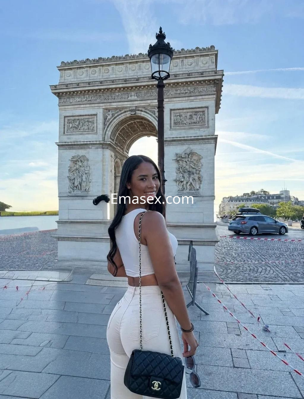 La puta posa de espaldas frente al Arco de Triunfo en Valencia, luciendo un conjunto blanco y una bolsa negra.