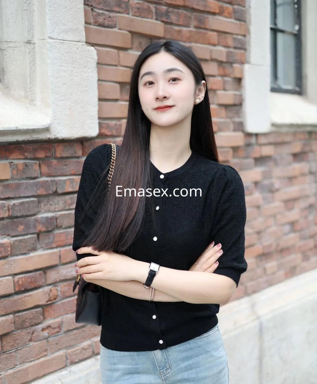 Puta de Zaragoza con cabello largo y lacio, vestida con un suéter negro y jeans, posando en una pared de ladrillos.