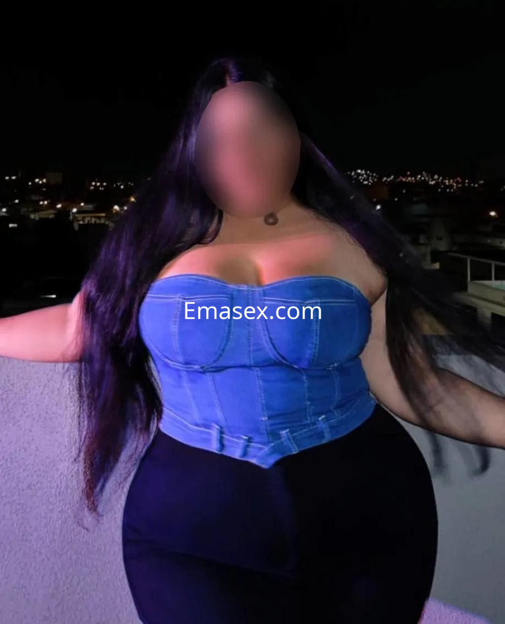 Puta con blusa de mezclilla ajustada y falda negra, posando en un balcón con luces de la ciudad de fondo en Zaragoza.