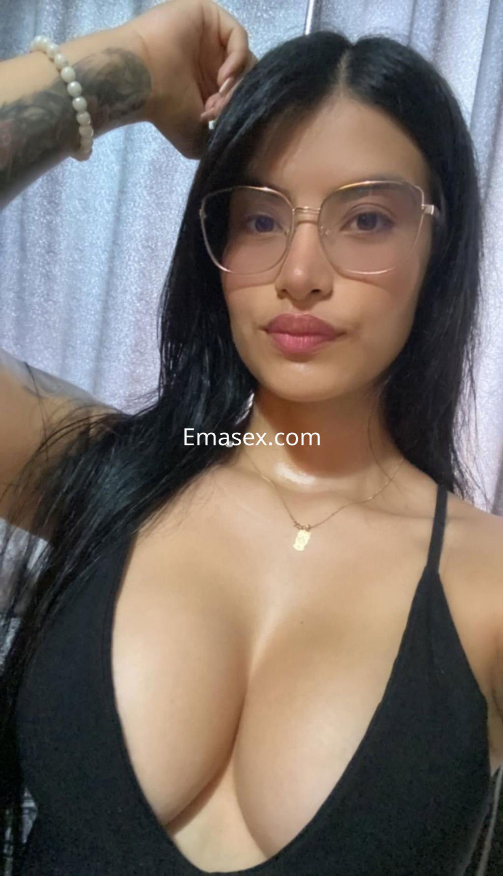 Puta en Zaragoza sonríe a la cámara con un top negro profundo y gafas, luciendo su cabello largo y lacio.