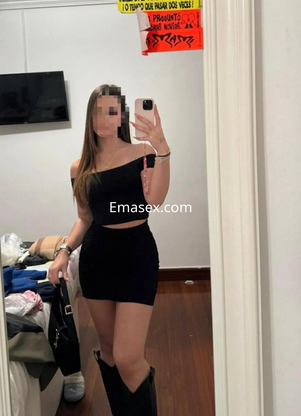 Puta en Zaragoza lleva un top negro sin mangas y una falda corta, posando con una bolsa en un espejo.