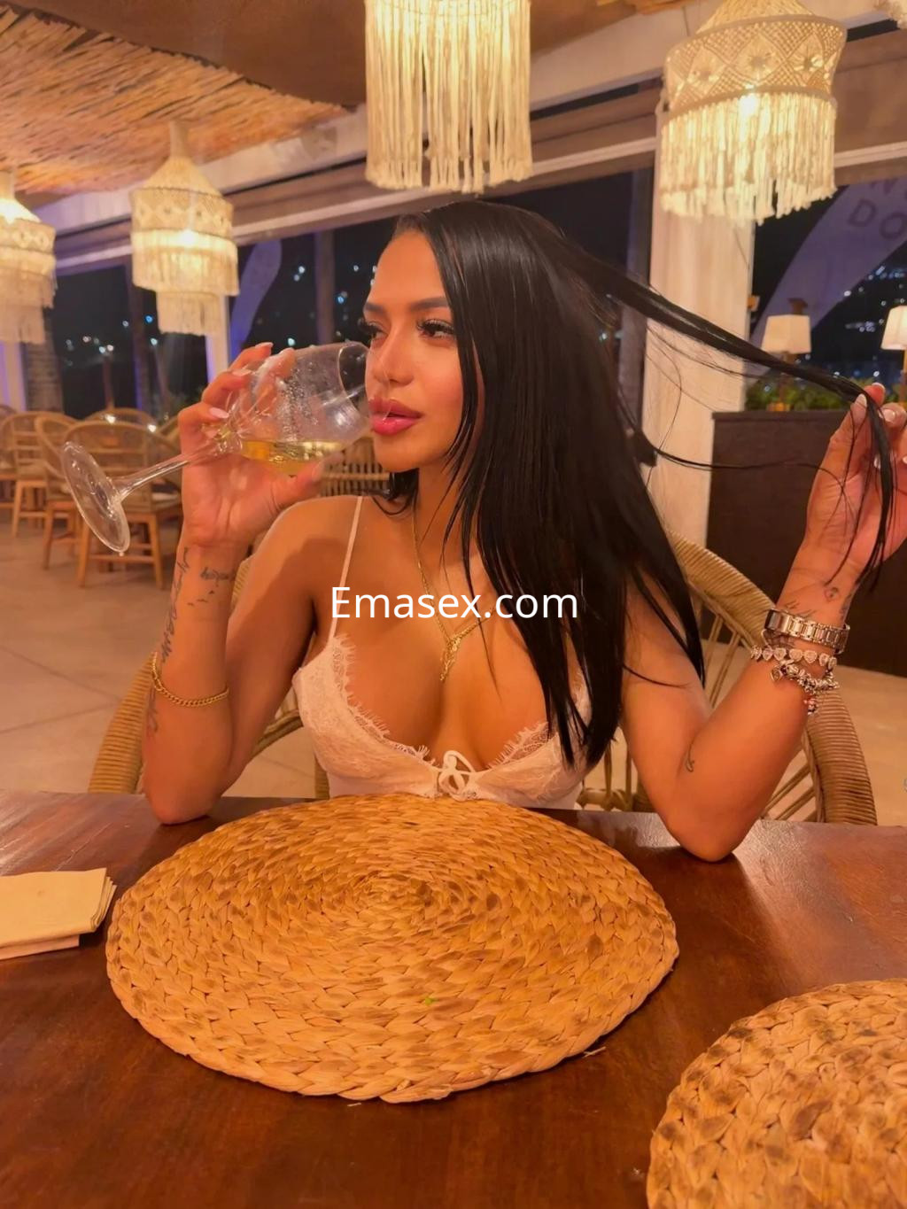 Escort en Zaragoza con top blanco, sosteniendo una copa en un restaurante con decoración acogedora.