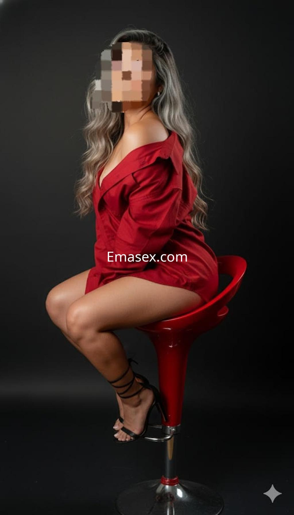 Puta sentada en una silla roja, viste una blusa roja amplia y tacones negros, con cabello largo y ondulado.