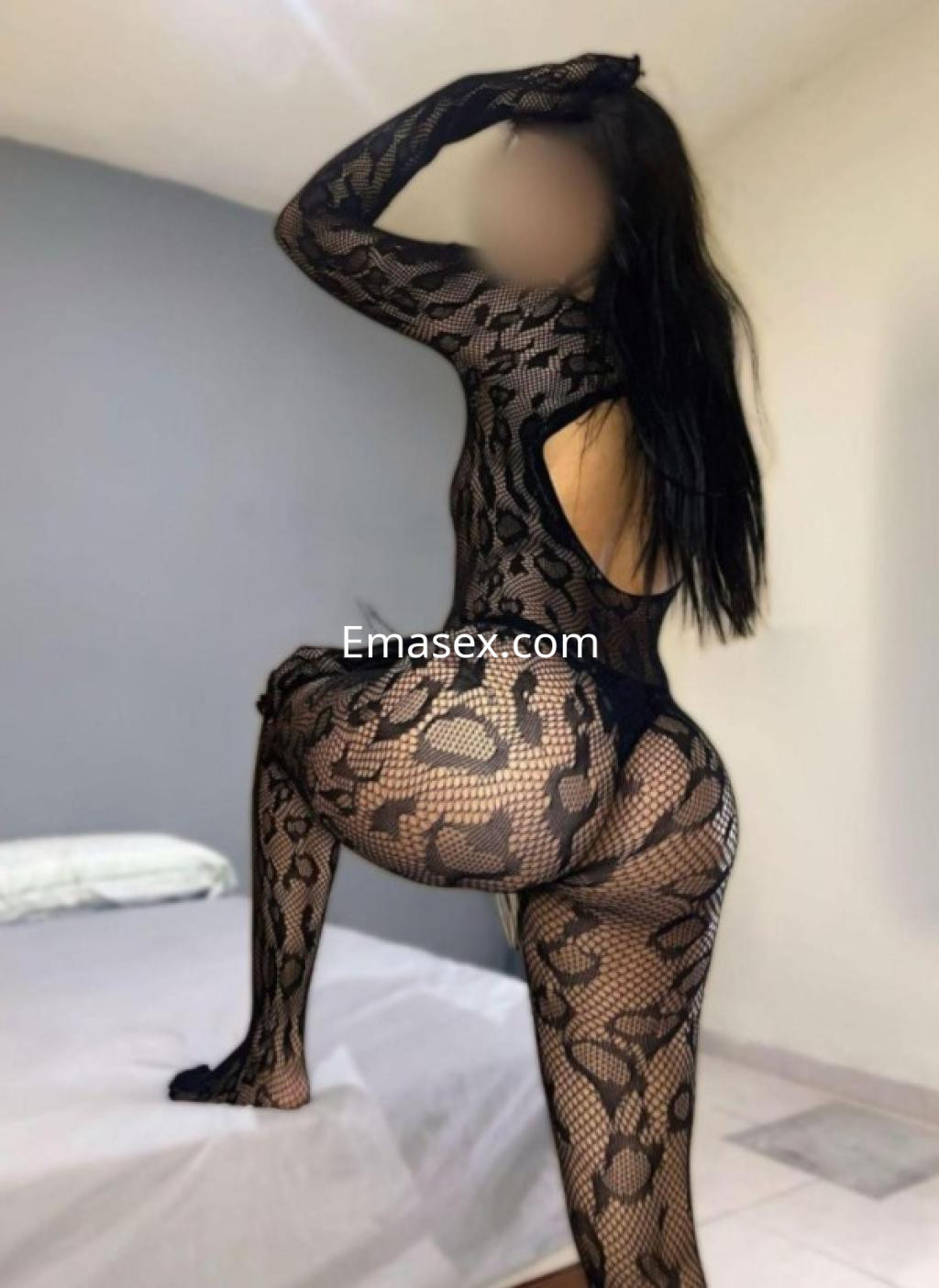 Escort en Logroño posando de espaldas con un body de encaje negro, resaltando su figura en un ambiente interior.