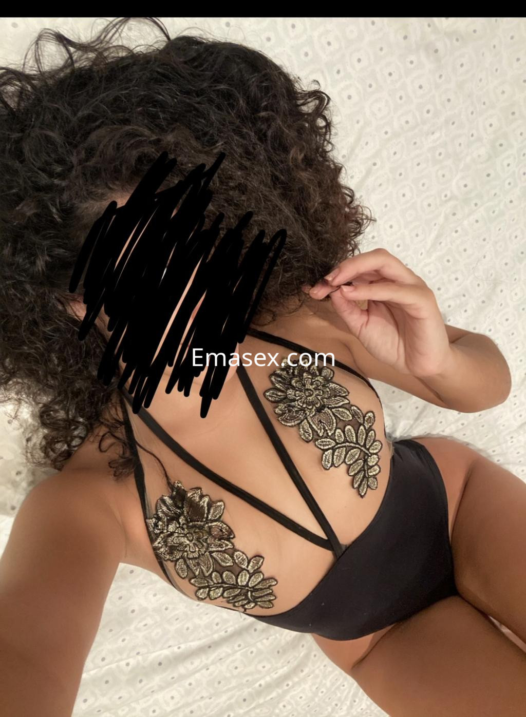 Escort en Málaga con cabello rizado, vistiendo un elegante bañador negro con detalles florales en la espalda.