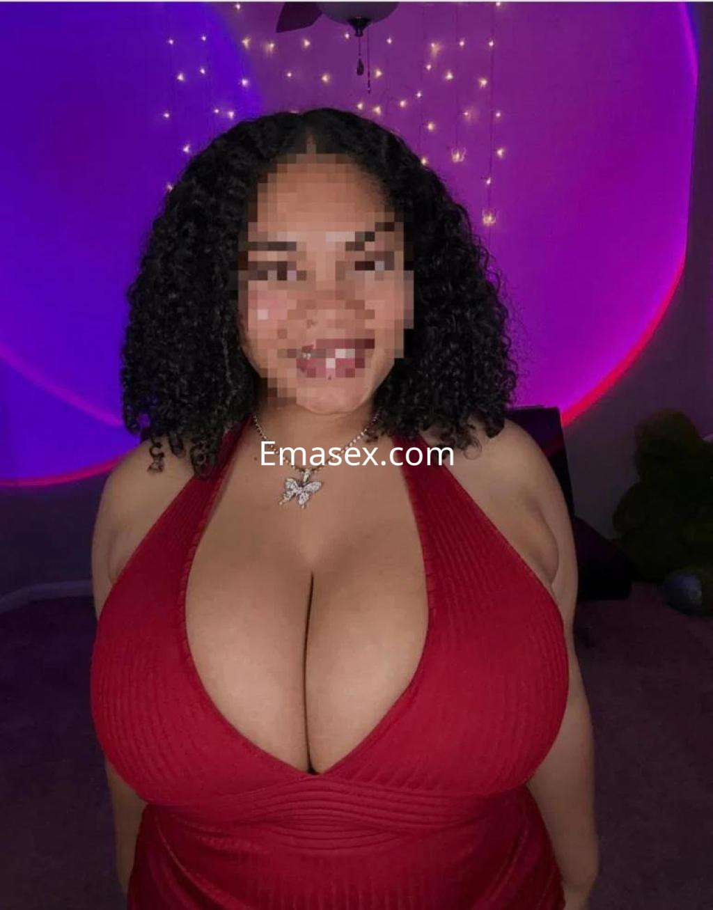 Escort en Cáceres con cabello rizado y vestido rojo, posando en un ambiente iluminado con luces suaves.