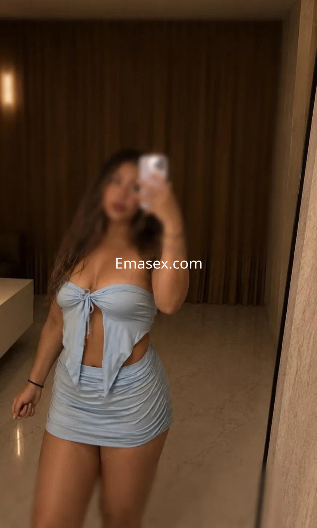 Puta posando en Cádiz con un top azul claro con nudos y una falda corta, mostrando una figura curvilínea.