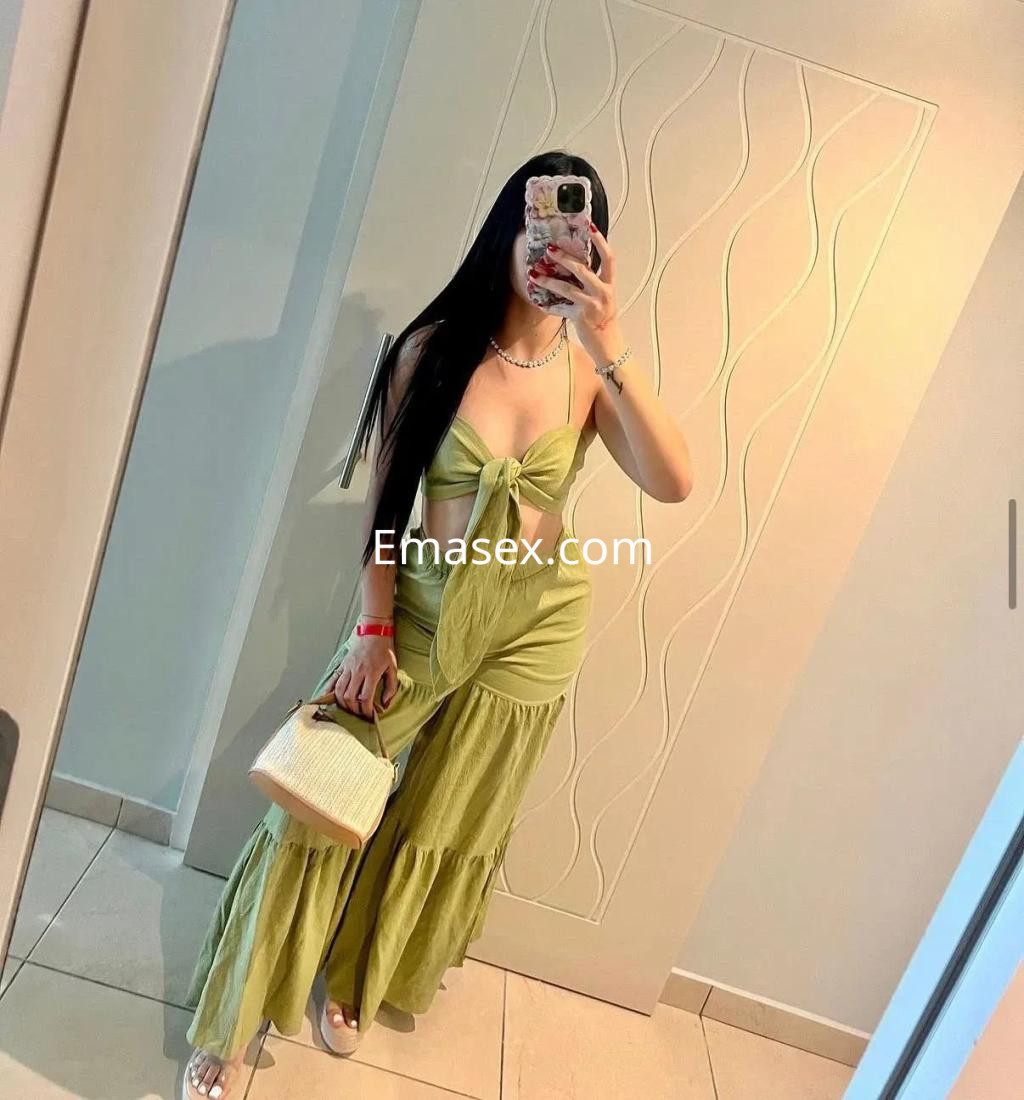 Escort en Cádiz con cabello largo y lacio, viste un conjunto verde claro de dos piezas y sostiene un bolso blanco.