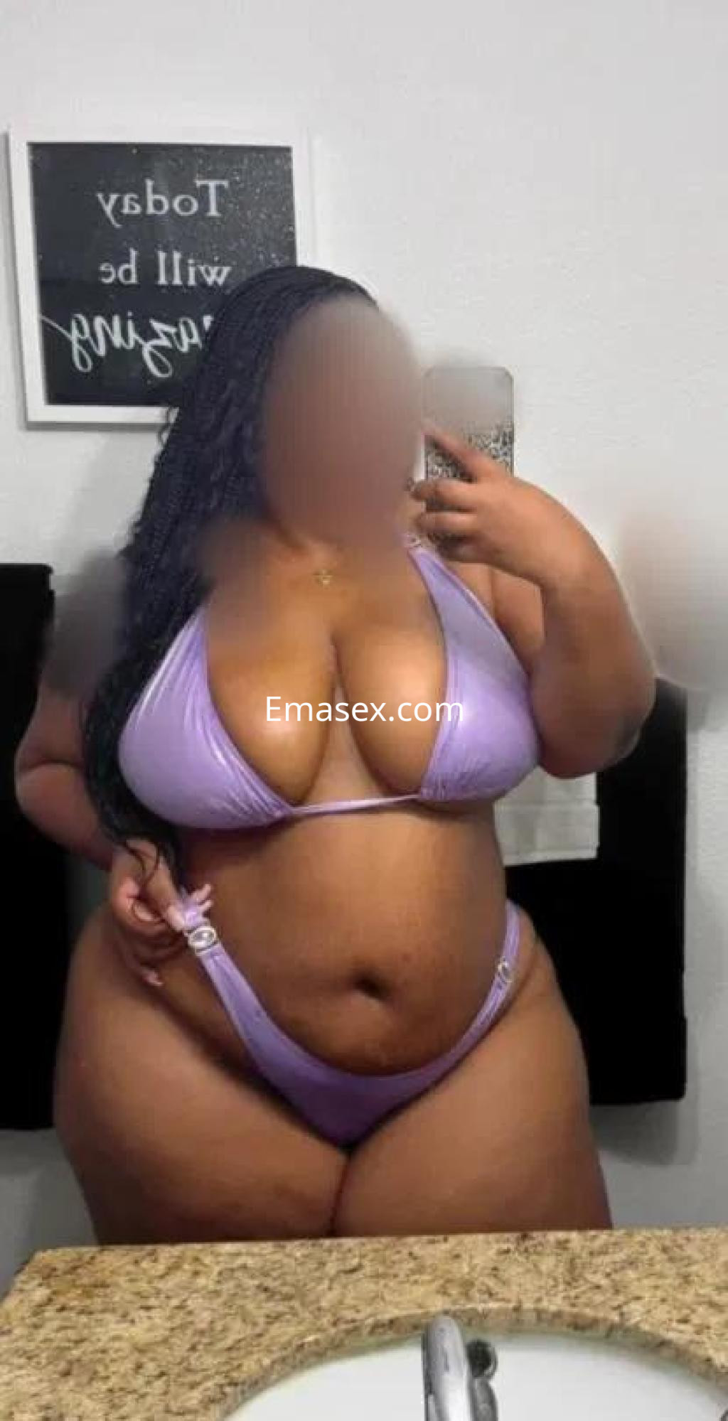 Escort en Huelva con cabello rizado, posando en un espejo con un bikini de color lila y fondo neutro.