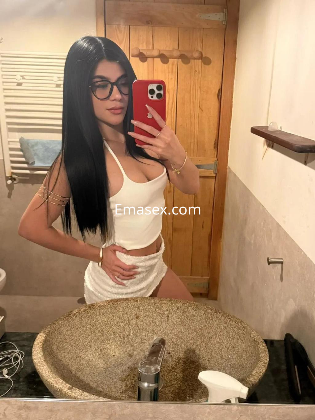 Puta en Málaga, posando frente al espejo con un vestido blanco ajustado y gafas, mostrando su cabello largo y lacio.