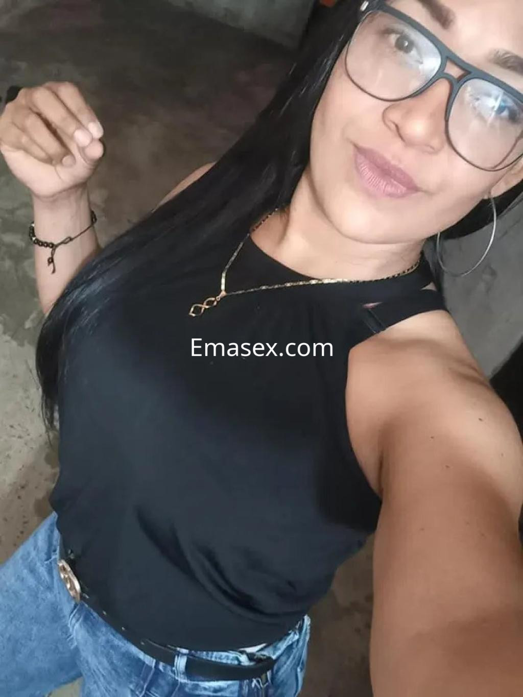 La puta viste una camiseta negra y jeans, posando con gafas en un entorno informal en Málaga.