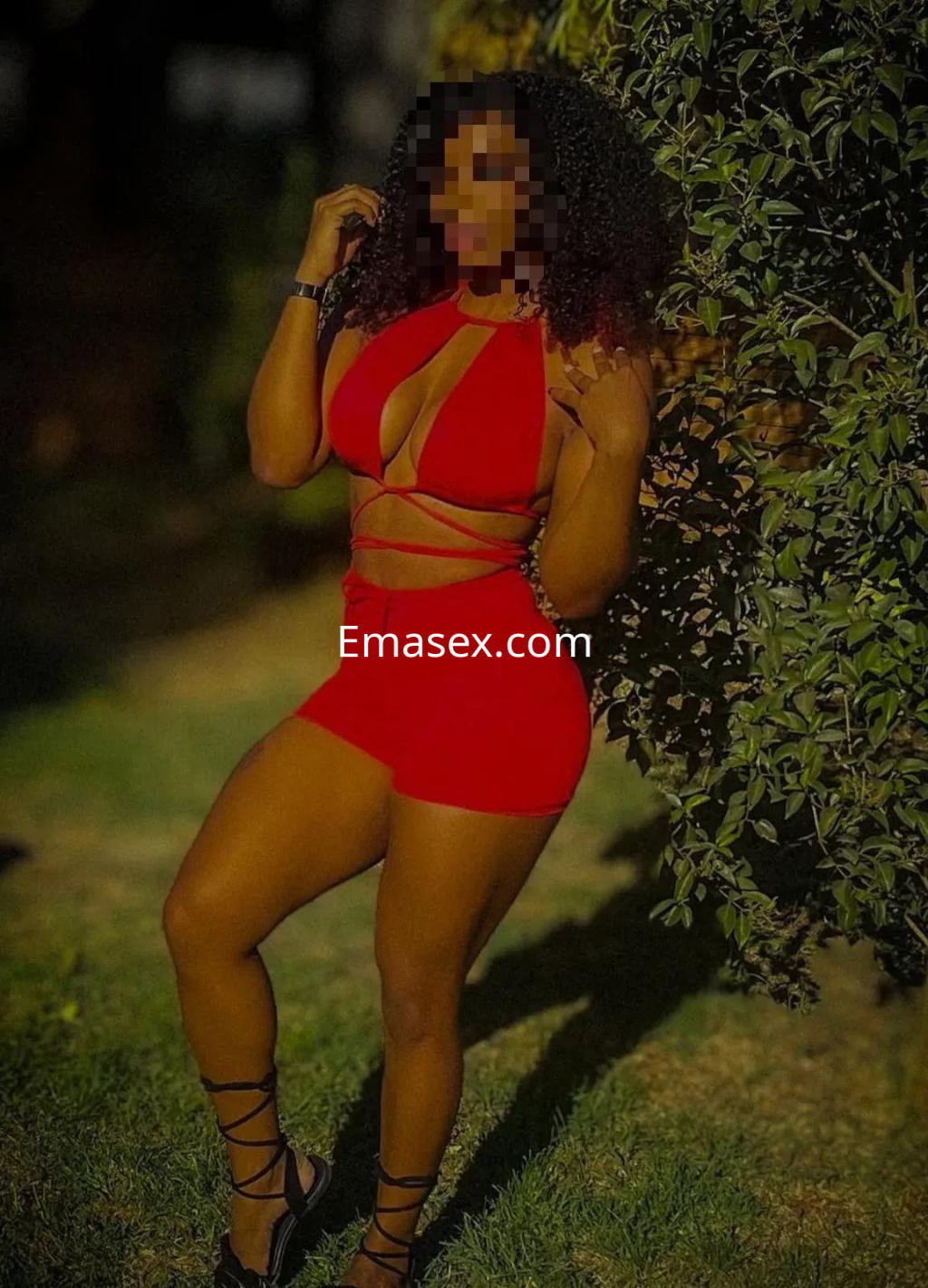 Escort en Málaga luciendo un vestido rojo ajustado con detalles en tiras, posando en un entorno natural.