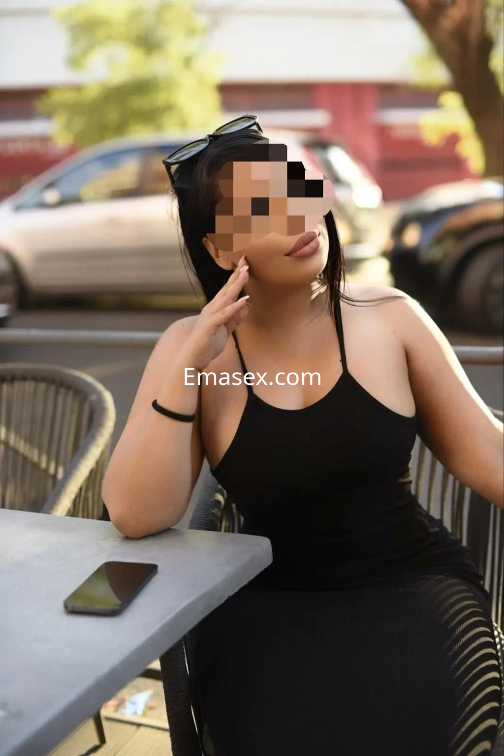 Escort sentada en una terraza de Sevilla, luciendo un vestido negro ajustado y gafas de sol.