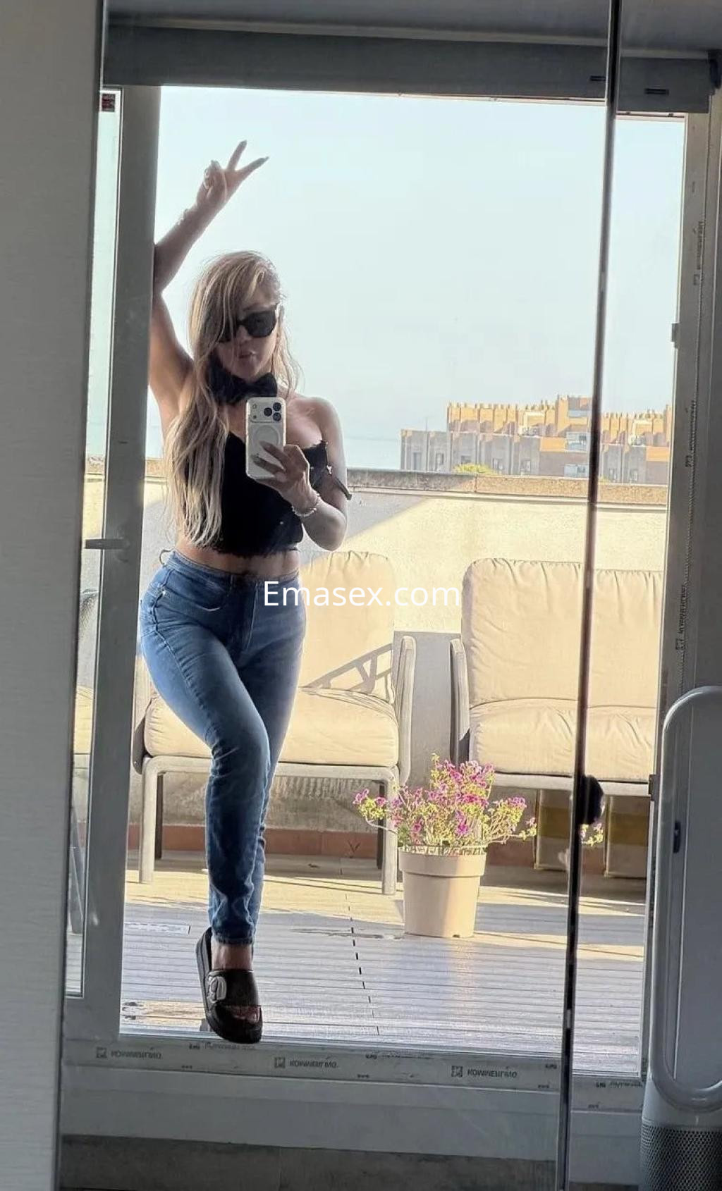Puta con cabello largo y rubio, vestida con top negro y jeans, posa frente a un espejo en Tarragona.