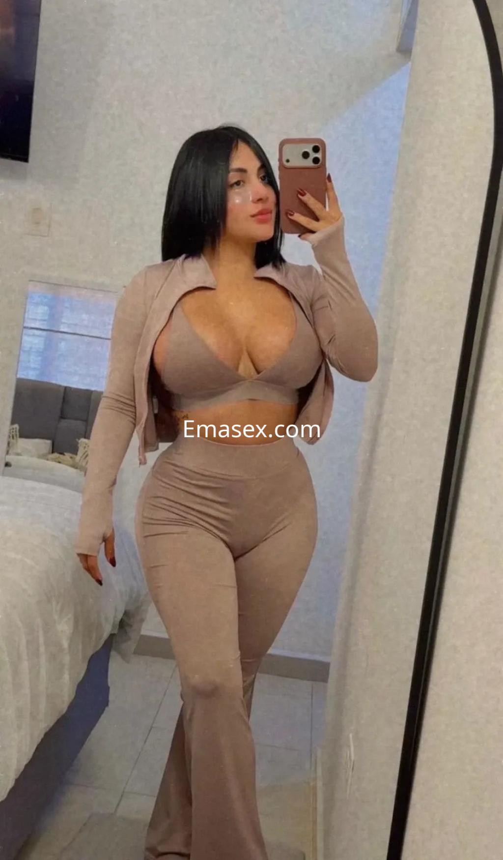 Escort en Zaragoza con cabello oscuro y lacio, vistiendo un ajustado conjunto beige frente a un espejo.