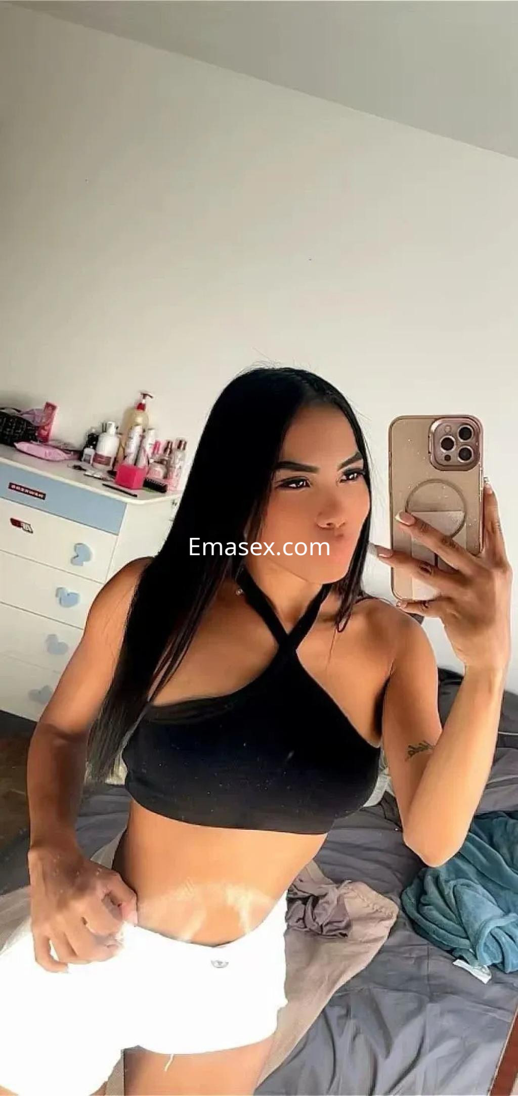 Puta en Coruña se toma un selfie frente al espejo, luciendo un top negro y pantalones cortos blancos.