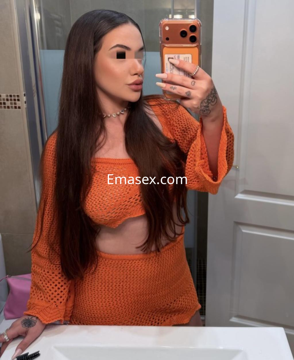 La puta en Vigo posa frente al espejo con un conjunto de punto naranja que resalta su figura y cabello largo.