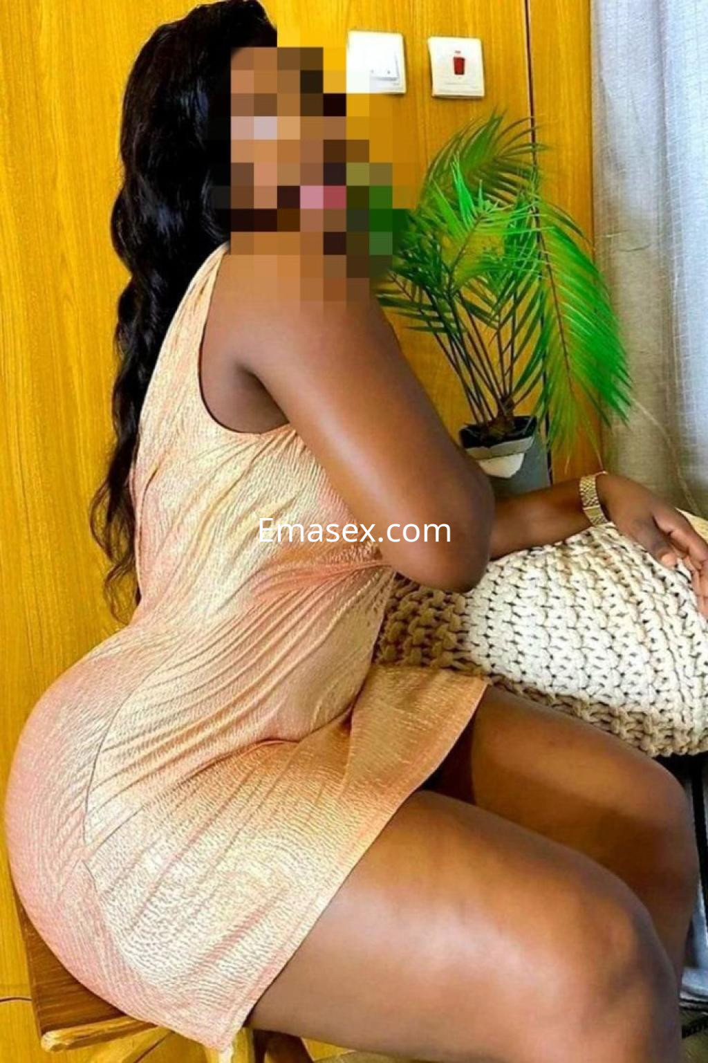 Escort en Zamora vistiendo un vestido ajustado de color dorado, posando de lado sobre una silla en un ambiente acogedor.