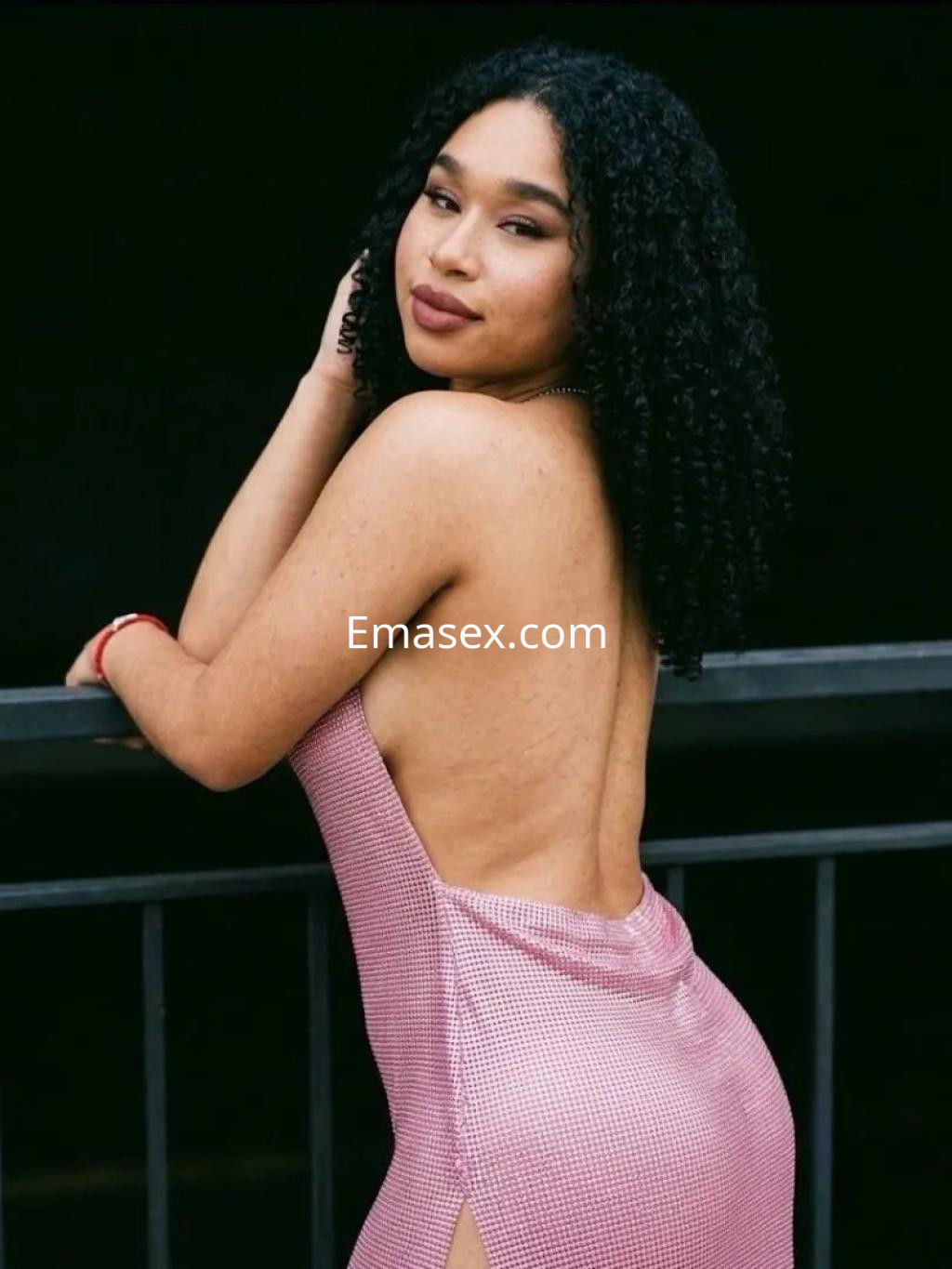 Escort en Alicante con cabello rizado y oscuro, viste un vestido sin espalda de color rosa con detalles en cuadros.