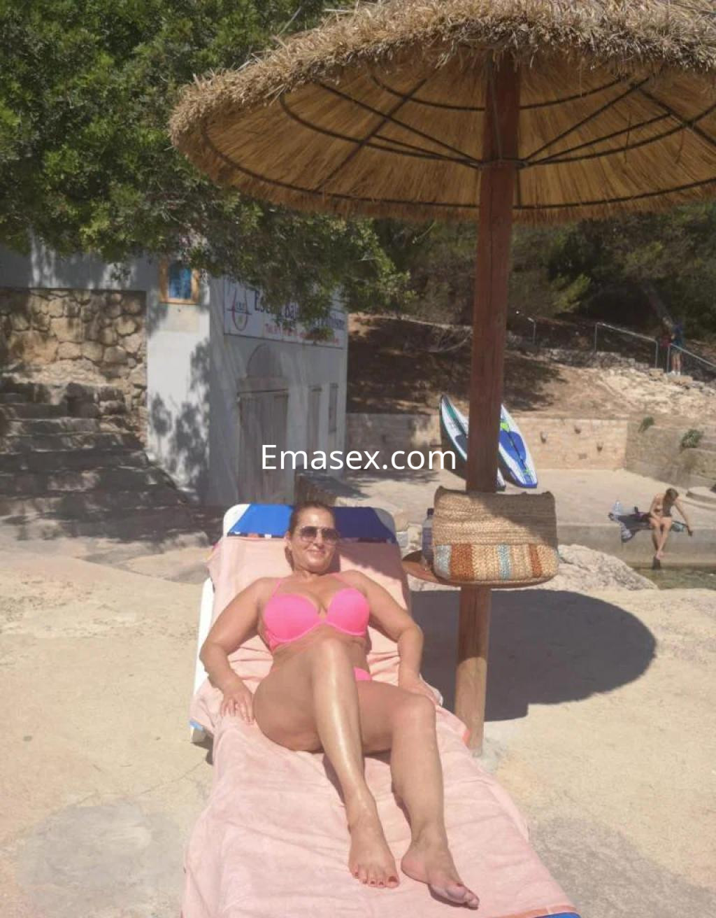 Puta en Palma de Mallorca, descansando en una tumbona bajo un sombrero, con bikini rosa y piel bronceada.